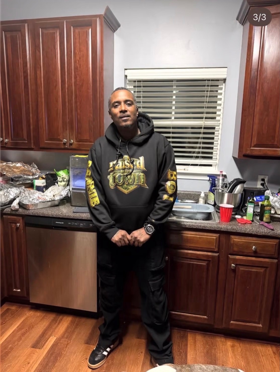 Person wearing a black hoodie with a gold raised by the town graphic