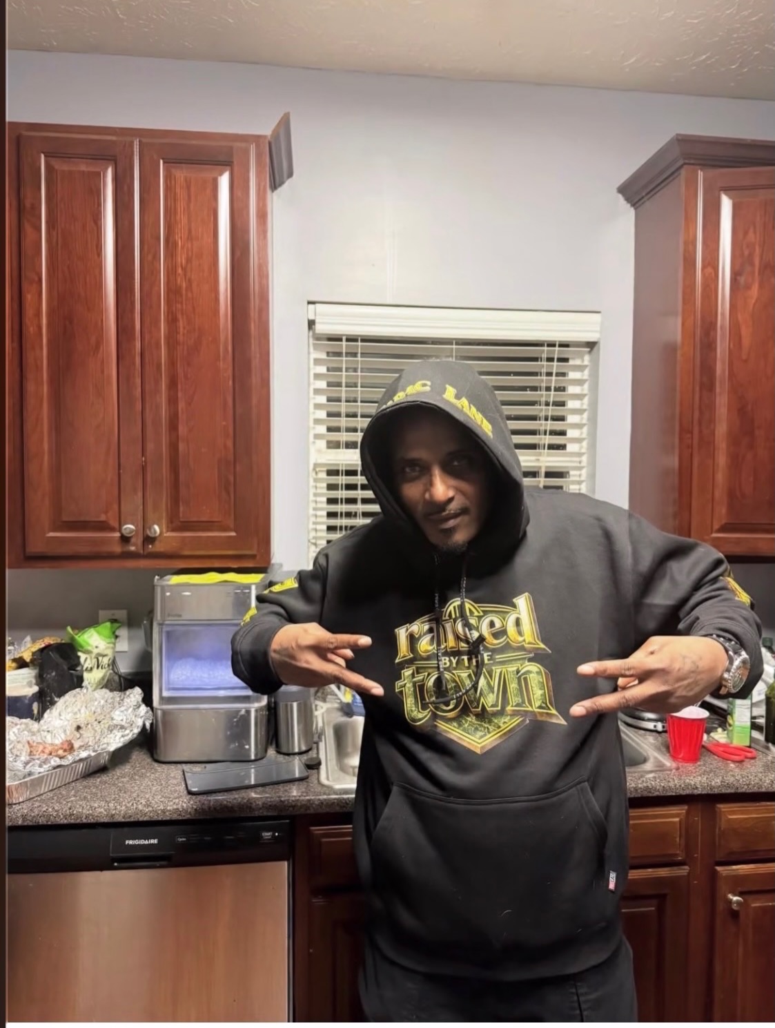 Person with hood up wearing a black hoodie with a gold raised by the town graphic
